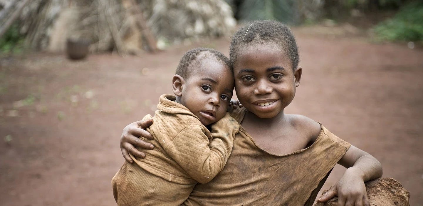 Ein Mädchen hält in Kamerun ein Baby im Arm. Beide schauen in die Kamera.