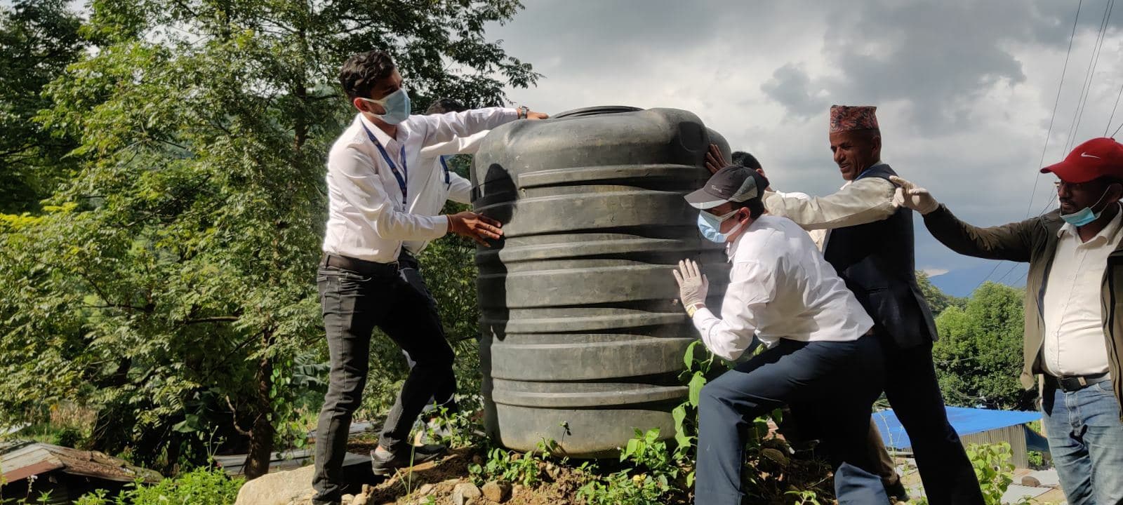 Trois hommes portant des masques et des gants vident un grand tonneau d'eau stagnante.