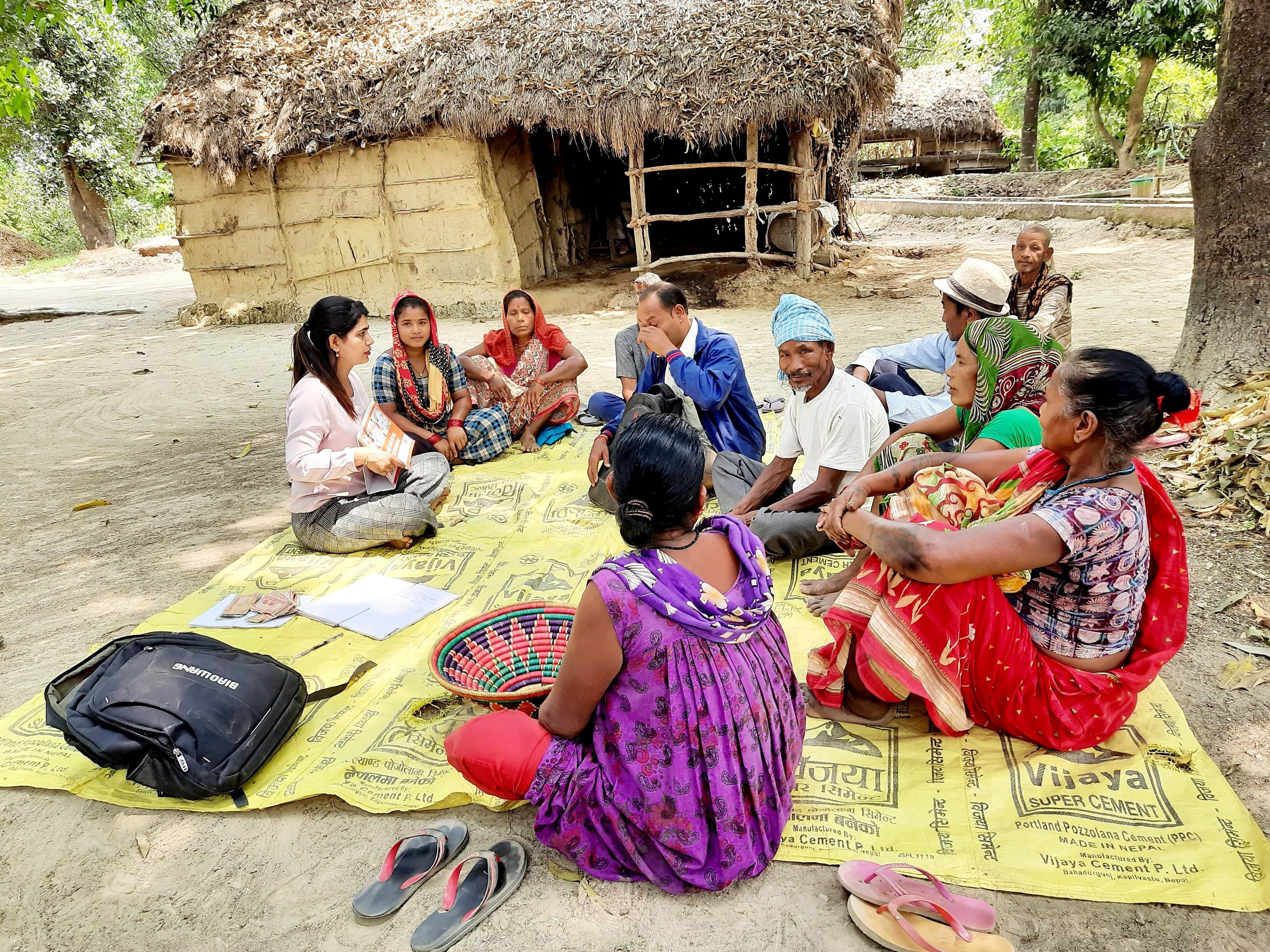FAIRMED-Gesundheitshelferin Sumitra Bhattarai sitzt im Freien undl eitet eine Selbsthilfegruppe, an der auch Soharatiya Tharu teilnimmt.