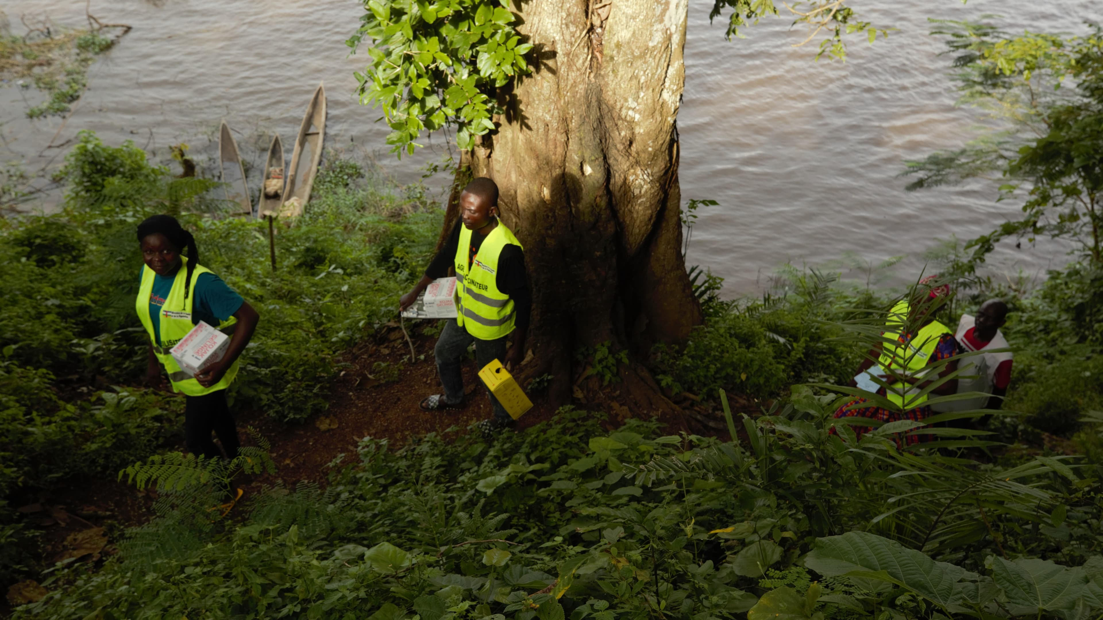 Auf dem Bild sieht man vier FAIRMED-Mitarbeitende, die gerade mit einem kleinen Boot angelegt haben und die Impfstoffe durch den Wald tragen.