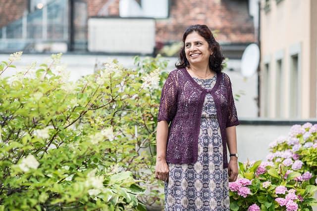 Auf dem Bild ist unsere Landeskoordinatorin für Nepal Nirmala Sharma zu sehen. Sie lächelt, trägt längeres schwarzes Haar und ein buntes Kleid mit einem lila Pullover darüber.