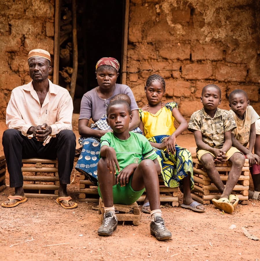 Eine Familie in Kamerun sitz vor einer Lehmhütte. Es sind Mutter, Vater und vier Kinder. Sie alle schauen in die Kamera.