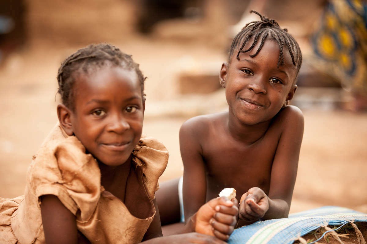 Two children in Bankim, Cameroon, lie on their bellies and laugh into the camera.