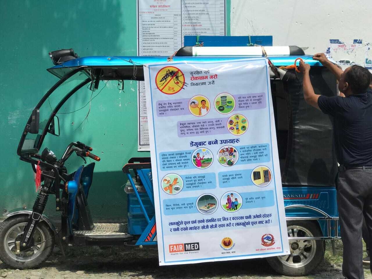 Une affiche sur la dengue est accrochée sur le côté d'un rickshaw motorisé.