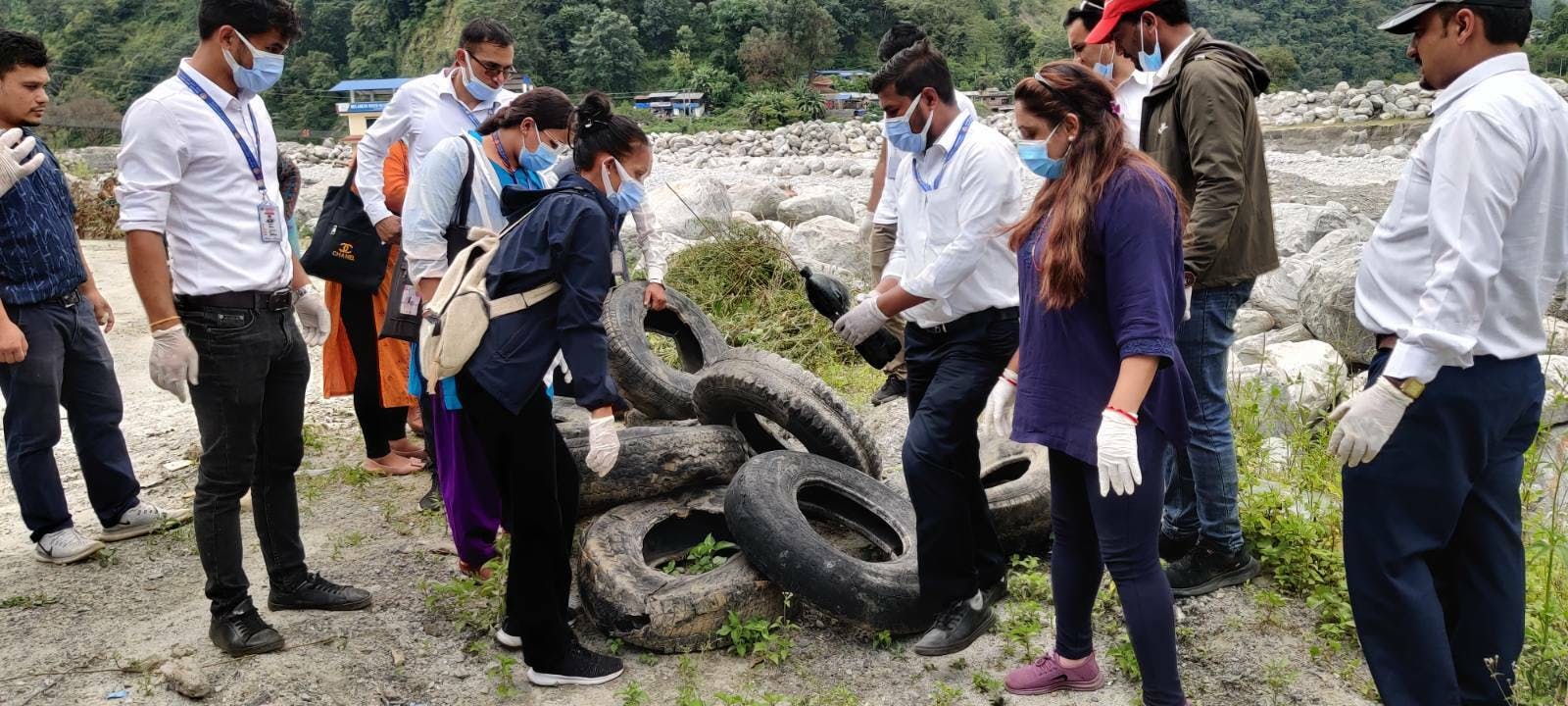 Différents acteurs portant des masques et des gants fouillent une pile de pneus de voiture à la recherche de larves. Ceux-ci sont empilés juste devant une rivière.
