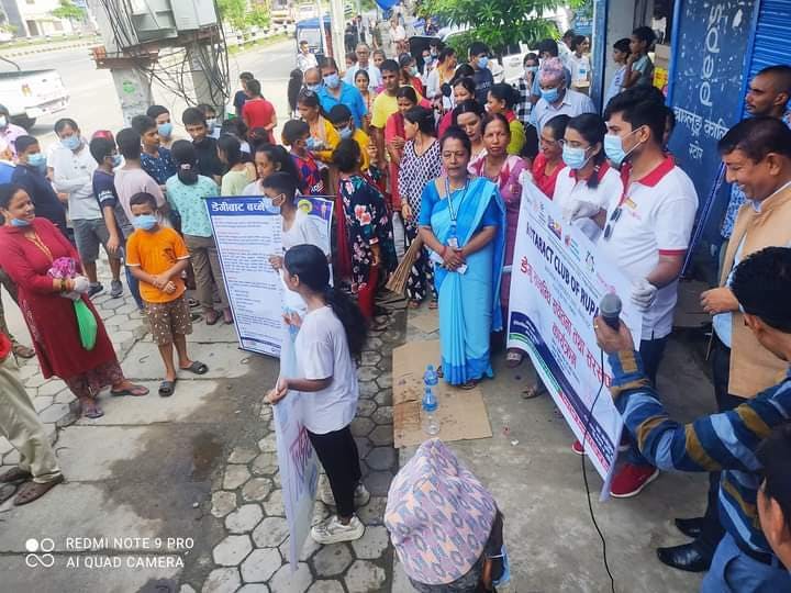 Des collaborateurs de FAIRMED se tiennent devant une foule de personnes et leur expliquent les mesures de prévention et les possibilités de traitement de la dengue. Certains tiennent de grandes affiches dans leurs mains.