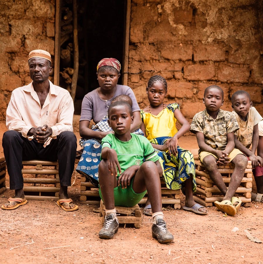 Une famille camerounaise est assise devant une hutte en terre. Il y a la mère, le père et quatre enfants. Ils regardent tous la caméra.