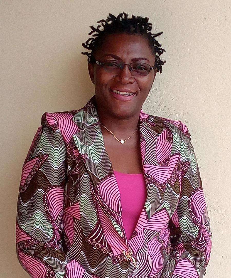 Notre coordinatrice nationale FAIRMED au Cameroun Marguerite Belobo. Elle porte un t-shirt rose et un blazer rose, vert et gris, ainsi que des lunettes. Ses cheveux sont courts et tressés.