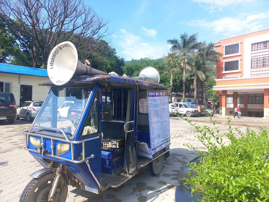 Une affiche sur la dengue est accrochée sur le côté d'un rickshaw motorisé. Celui-ci est équipé de haut-parleurs sur le toit.